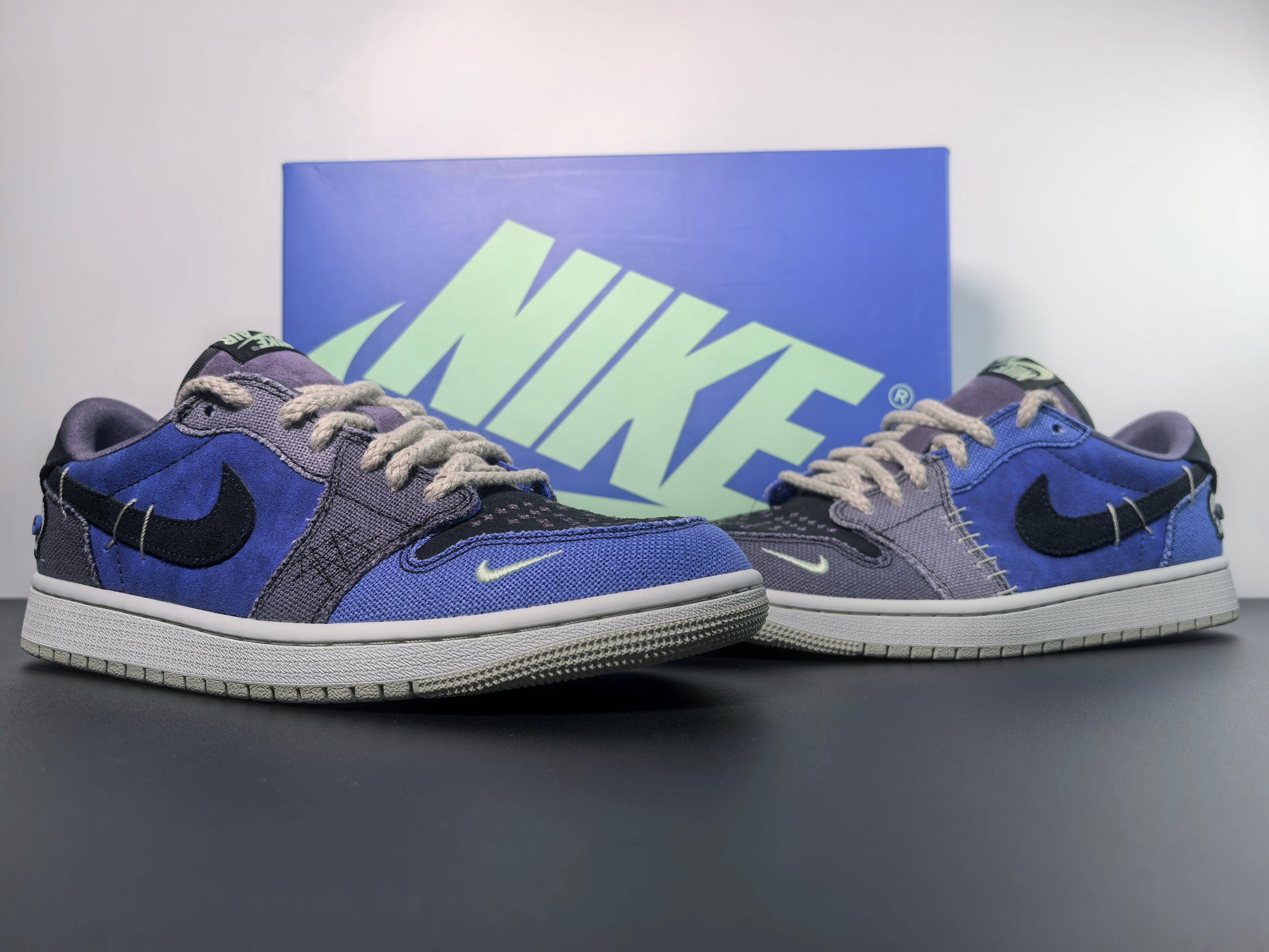 Premium Nike sneakers in blue and grey with black swoosh, showcased with branded box on black table